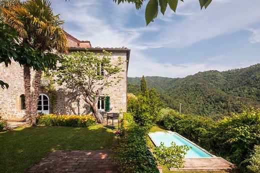 Italian farmhouse on hill with pool surrounded by green trees